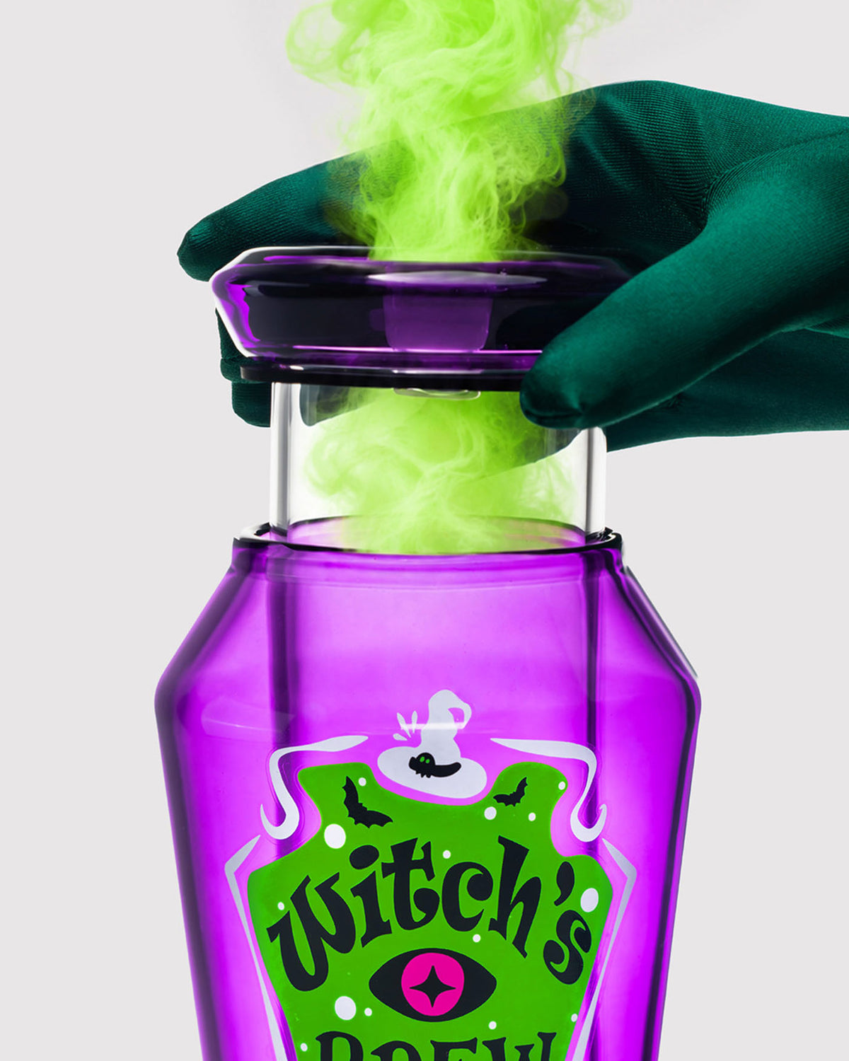 green gloved hand pushing down witch's brew gravity bong and releasing green smoke