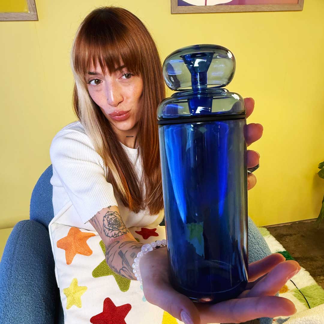model sitting on blue fuzzy chain and holding a blue glass gravity bong 