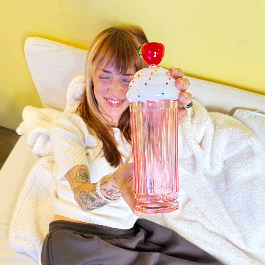Model laying on white couch with white fuzzy blanket showing off a milkshake gravity bong 