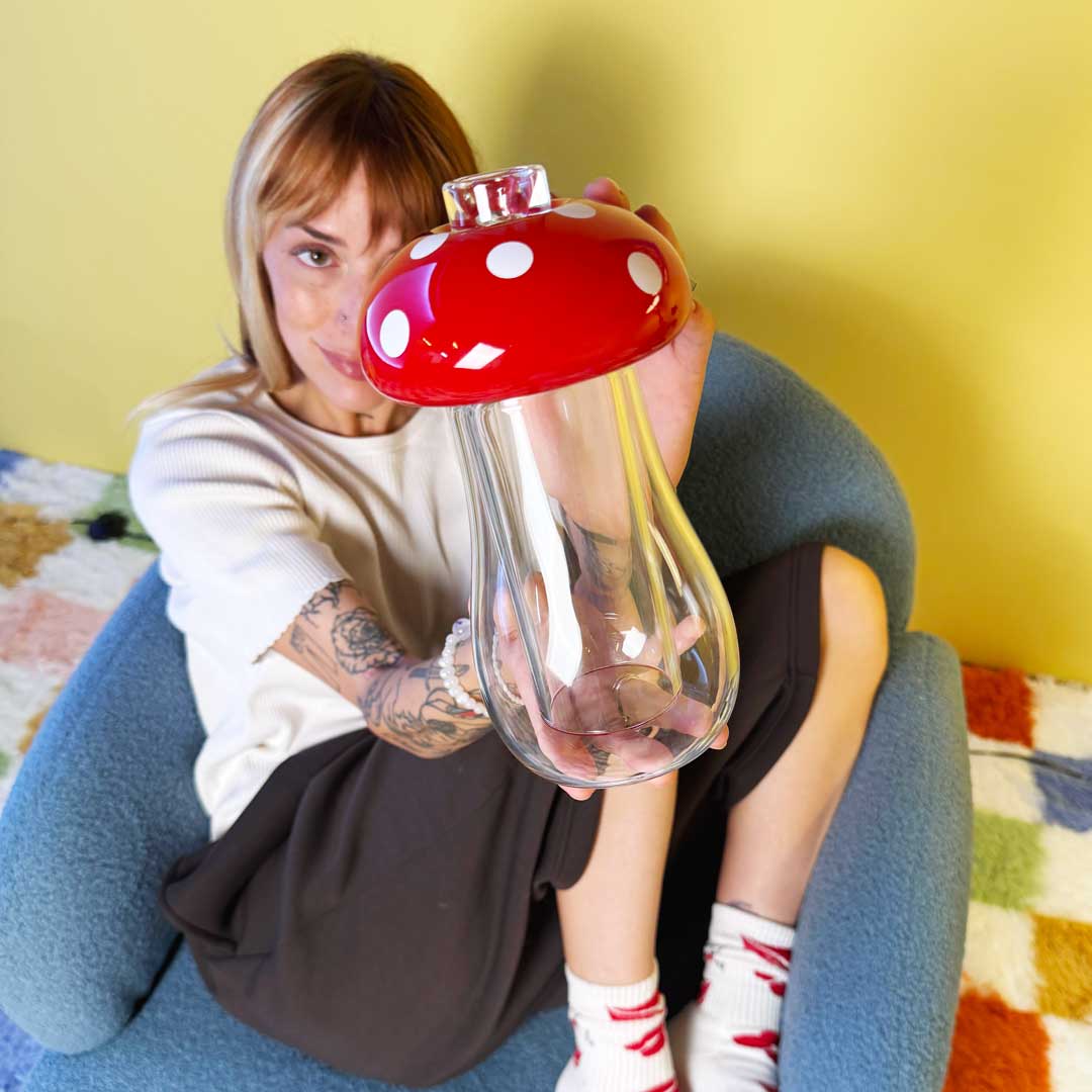 model sitting on blue lounge chair and showing a mushroom gravity bong
